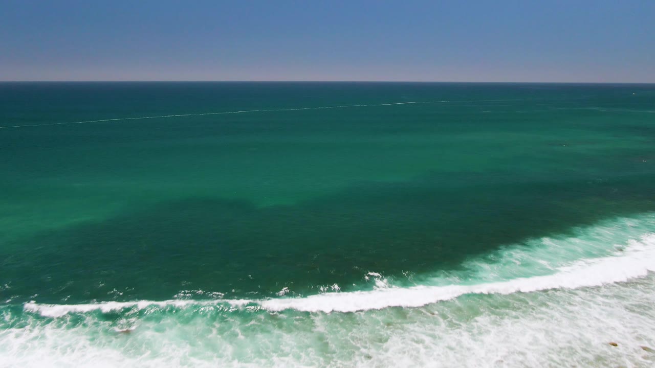 Aerial view of dark green ocean with white surf near the bottom edge