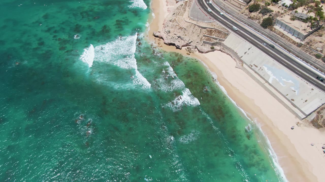 White waves breaking beside a sandy beach and road