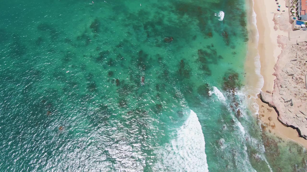 Sunlit ocean surface with underwater rocks and sandy shoreline