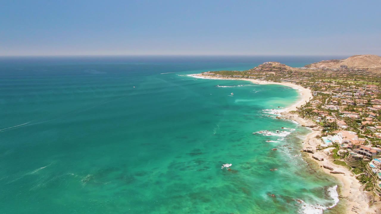 Turquoise water and curved beach with buildings lining the right side of the shore.