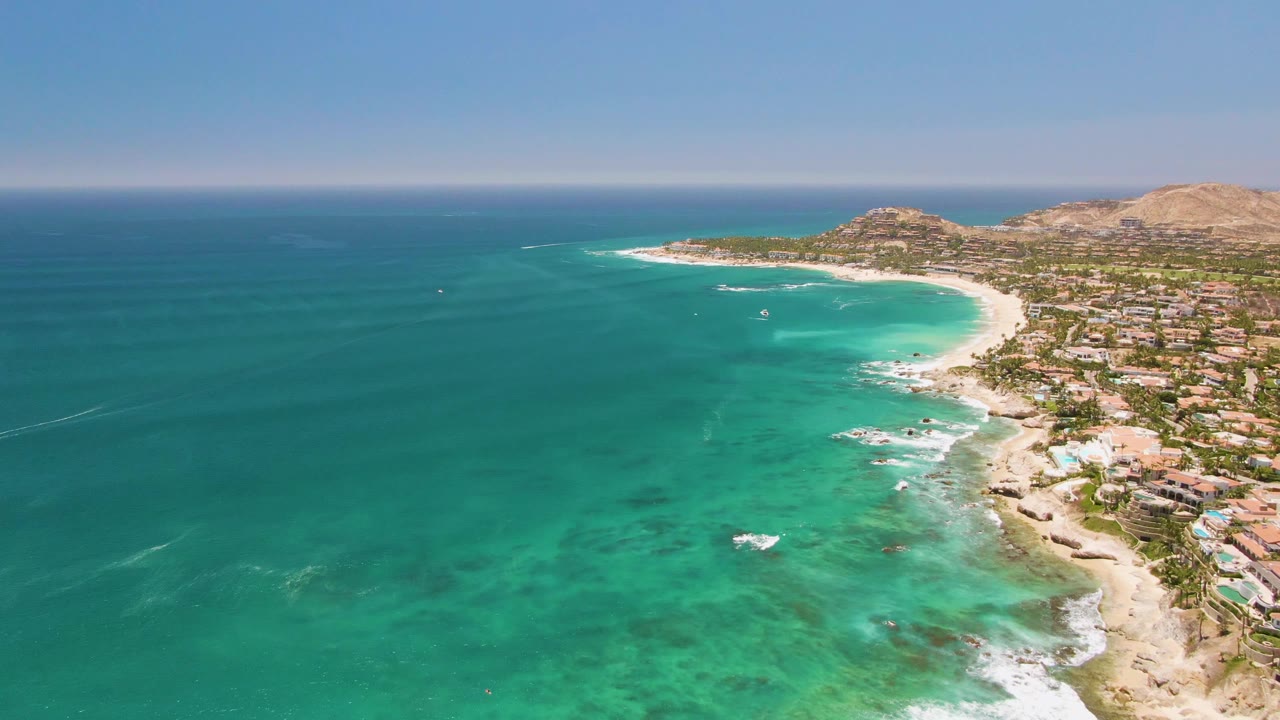 Wide aerial view of ocean, beach, shoreline buildings, and distant hills.