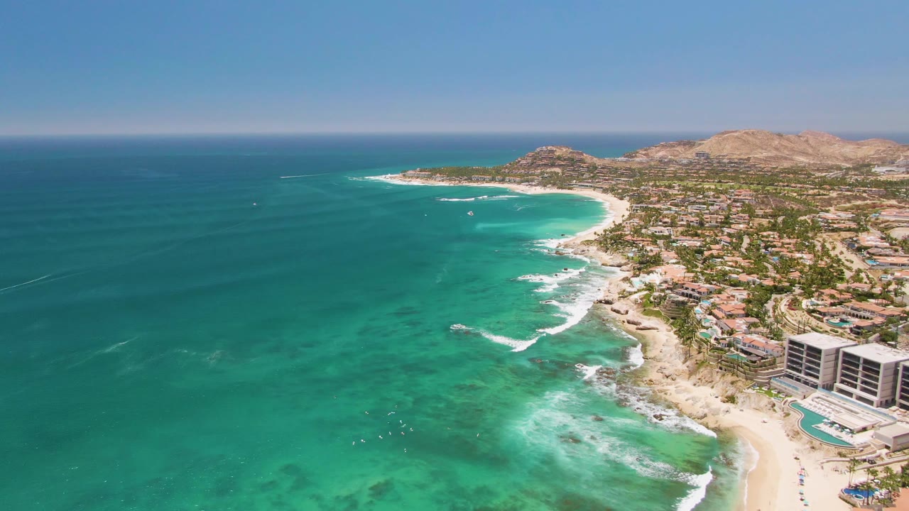Drone view of white surf curling beside beachfront buildings