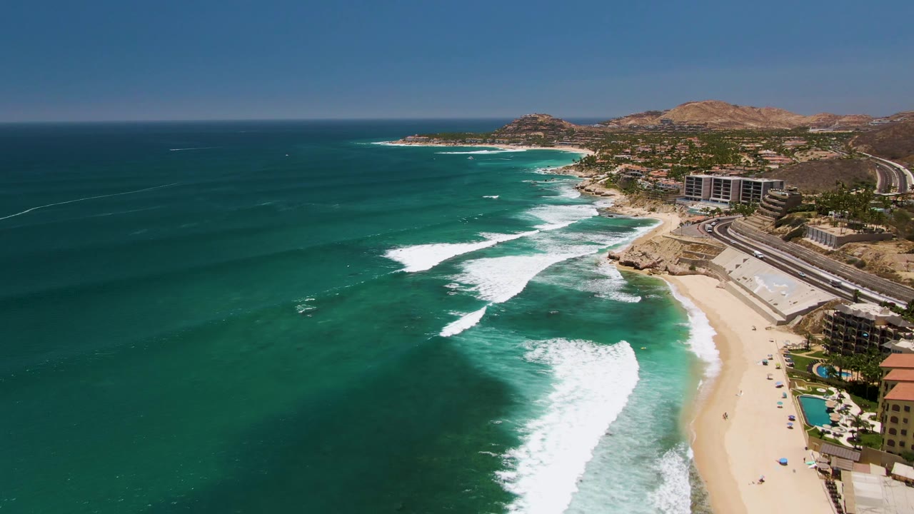 At two seconds, white foam sits closer to the lower shoreline while the Costa Azul Beach resort area, road, arid hills, and blue horizon remain visible in the background.