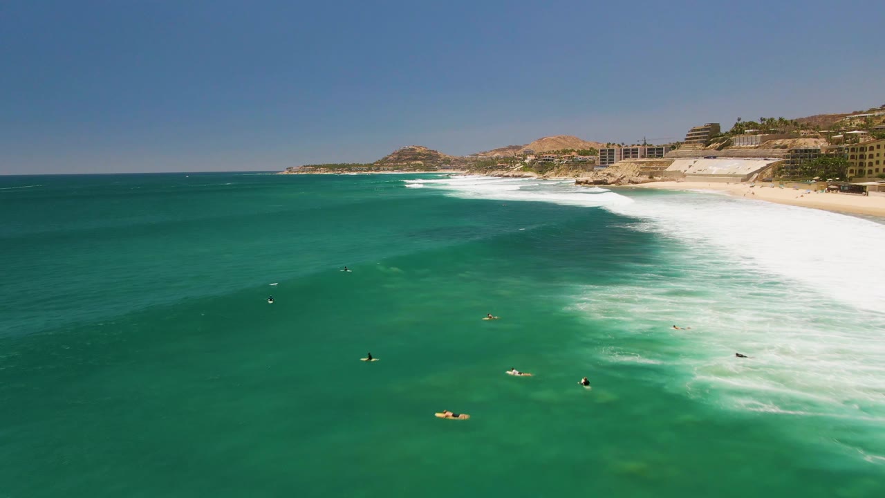 Turquoise water with small surfers and swimmers near rolling white waves