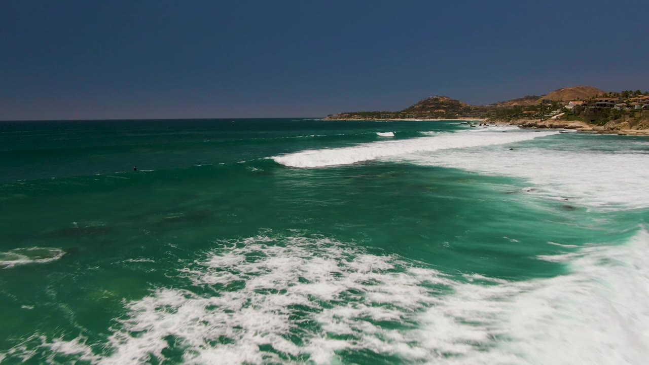 White surf spreads across turquoise water with small people offshore.