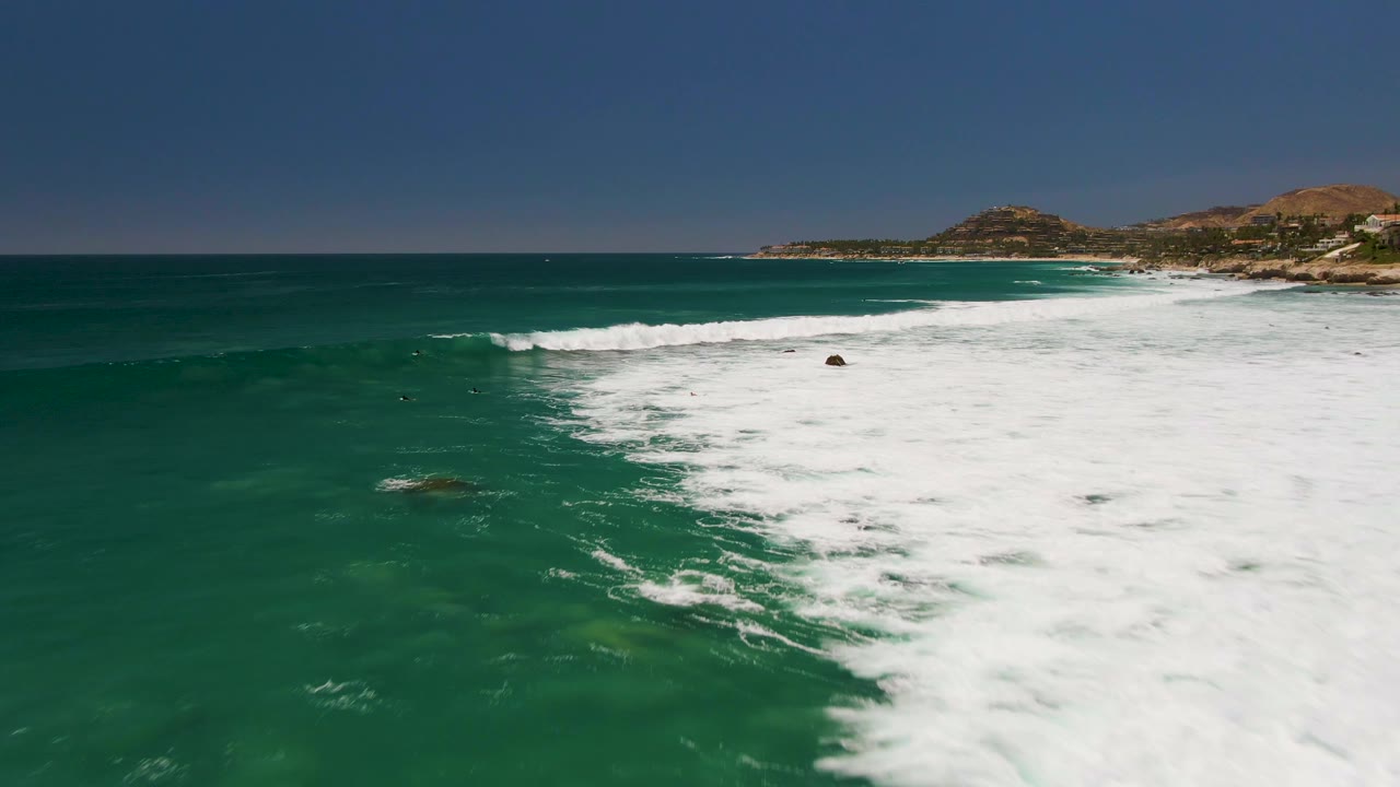 Foamy surf spreads over shallow rocks beneath a blue coastal horizon.