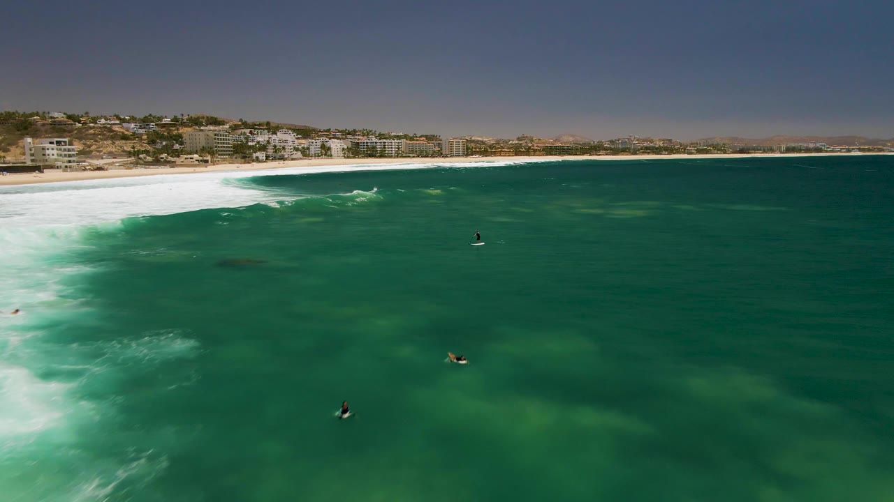 White wave wash curls along the shoreline with surfers farther offshore.