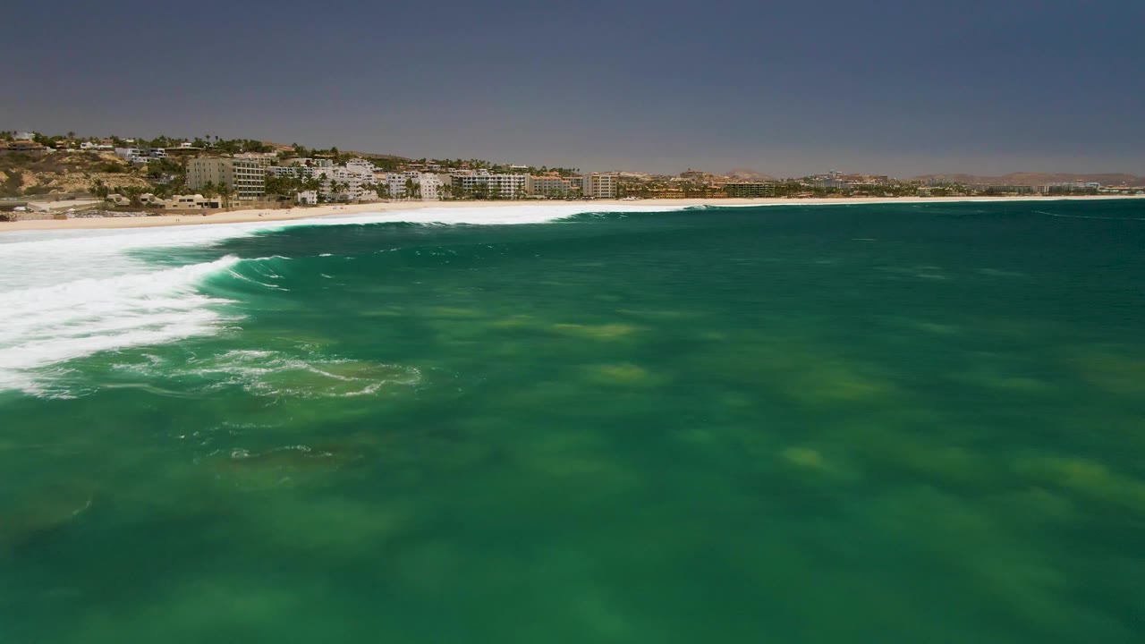 Wide green ocean surface with white surf curling toward a sandy shoreline.