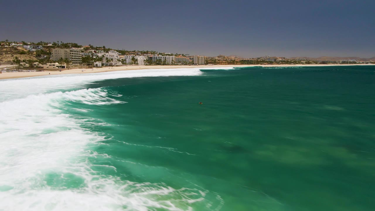 Wide aerial shoreline view with white surf and green ocean water