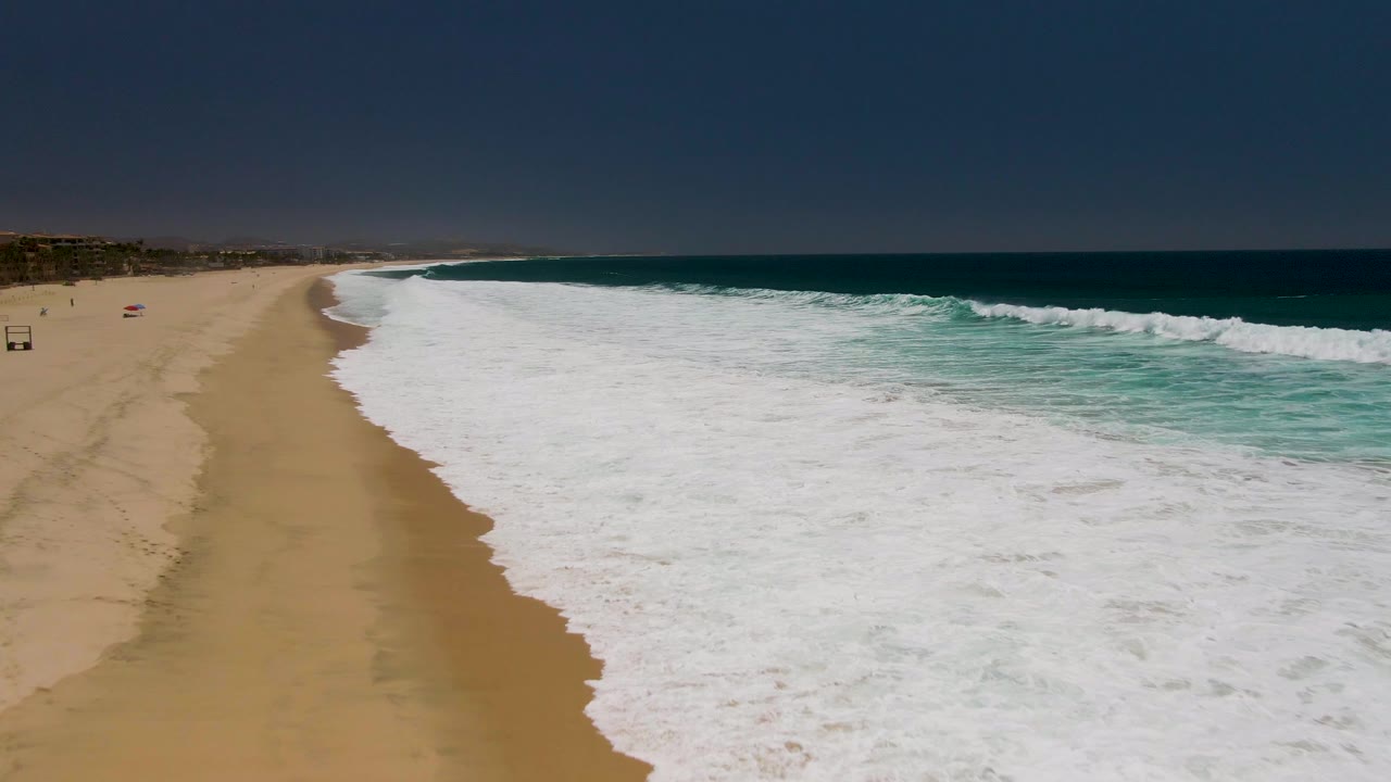 White ocean foam spreads over sand beside turquoise water