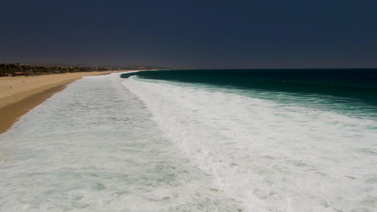Foamy waves cover the nearshore water along a sandy beach and blue ocean.