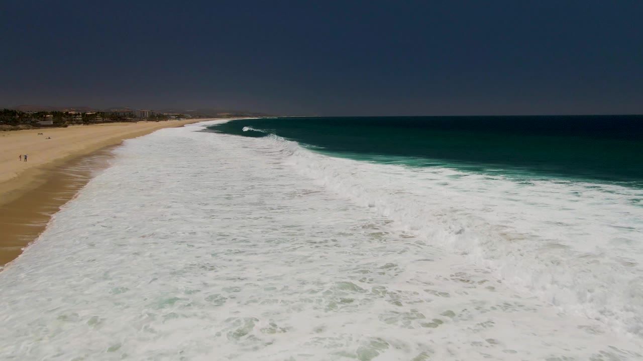 White waves break along a sandy shoreline with ocean water on the right.