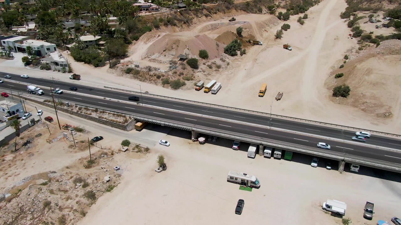 Cars move along a highway near an underpass and construction dirt.