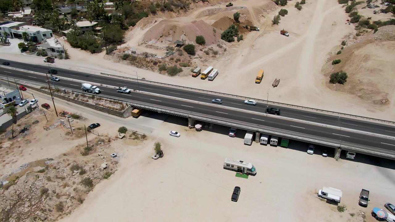 A highway overpass cuts across a dusty construction area with light traffic.