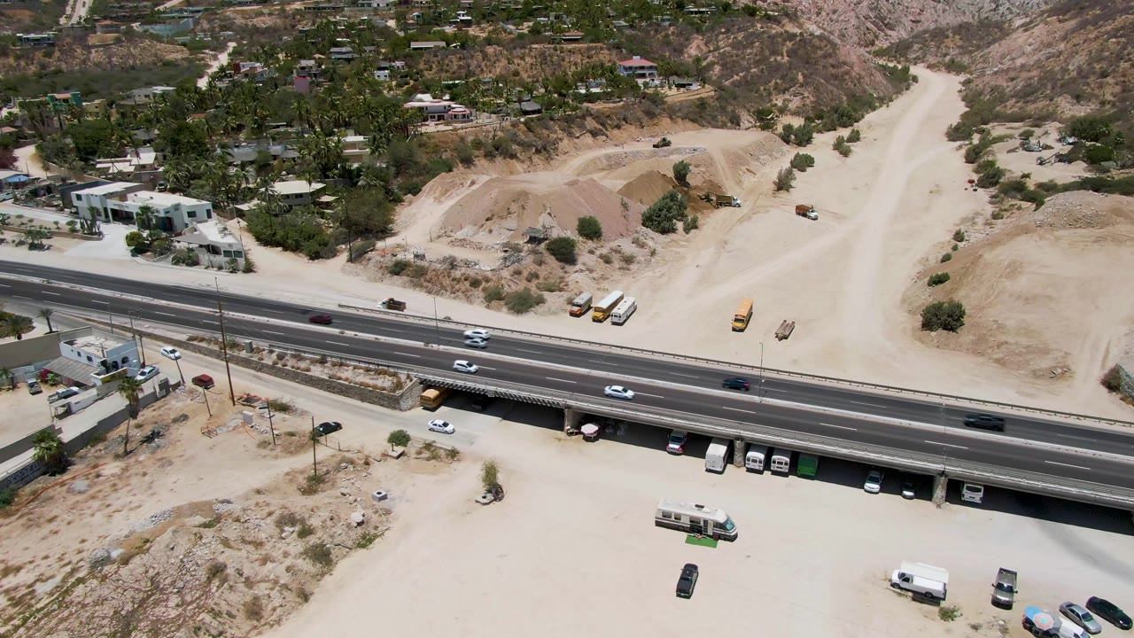 Aerial highway scene with vehicles, parked vans, dirt roads, and dry hills.