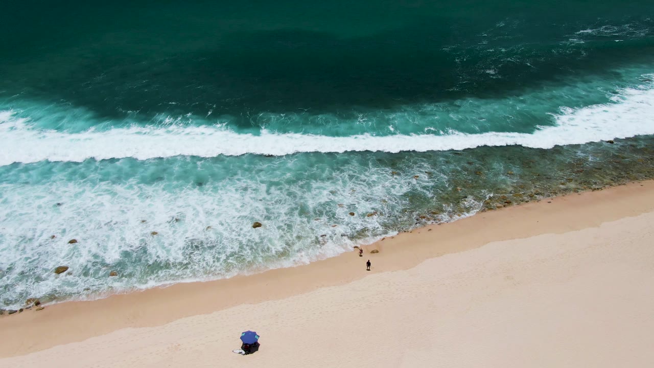 White waves break across a sandy beach with two walkers below.