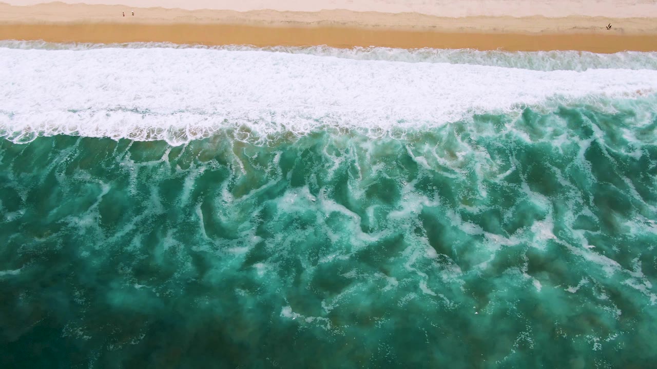 Overhead green ocean waves breaking toward a sandy beach
