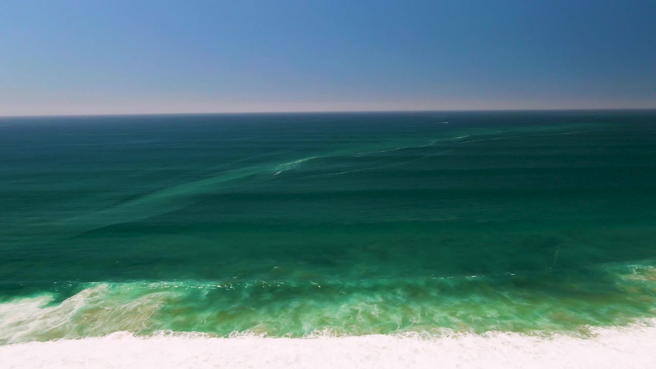 Aerial view in San Jose del Cabo with a level horizon, darker offshore water, pale turquoise wave bands, and no visible people or structures.
