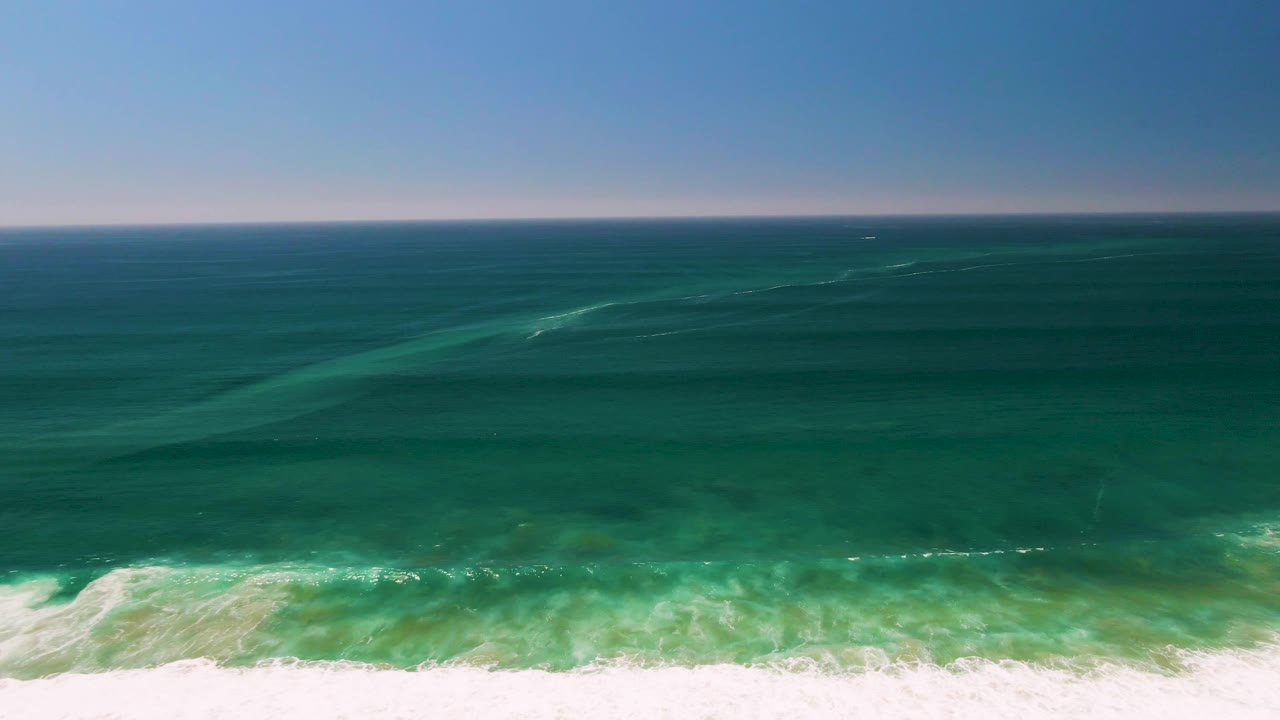 San Jose del Cabo ocean frame with deep teal water across the center, a pale foam strip along the bottom, and empty sky above the horizon with no visible people.