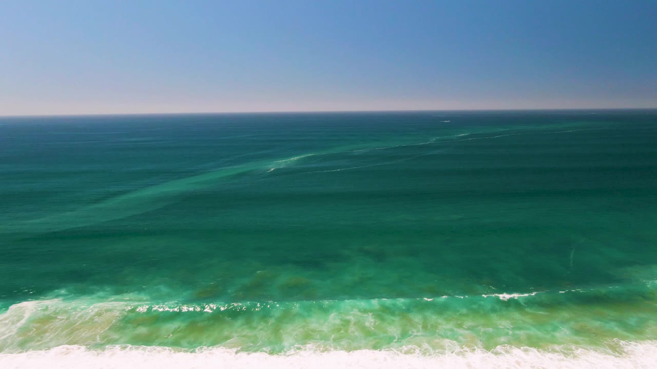 Aerial frame from San Jose del Cabo showing darker offshore water, a green wave line in the midground, and white surf at the foreground with no visible people.