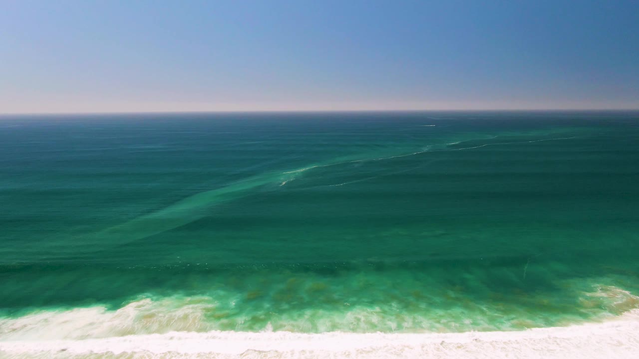 Aerial view of blue-green ocean waves breaking on pale sand