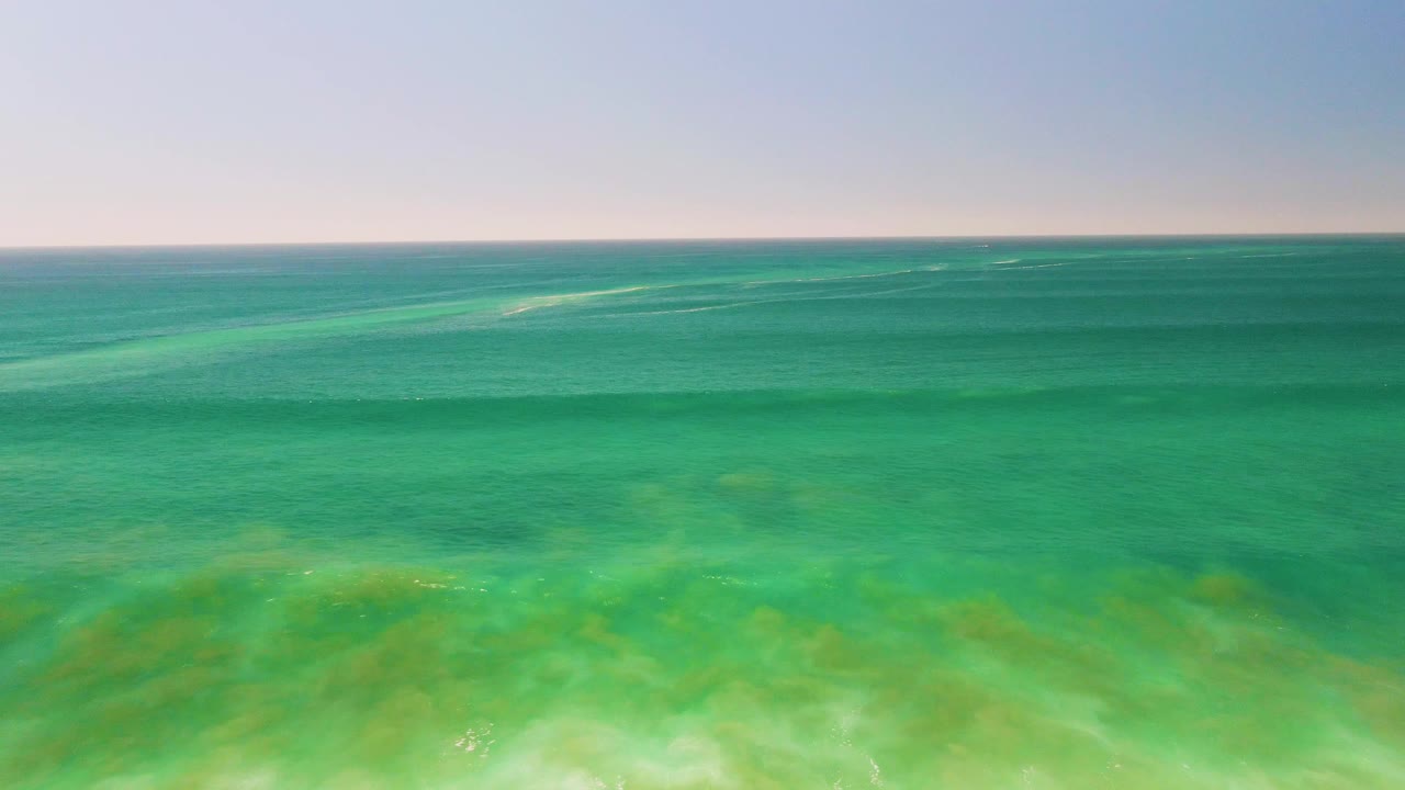 Mid-clip frame shows shallow turquoise water near San Jose del Cabo, with brighter foam and sand tones at the bottom and no visible people.