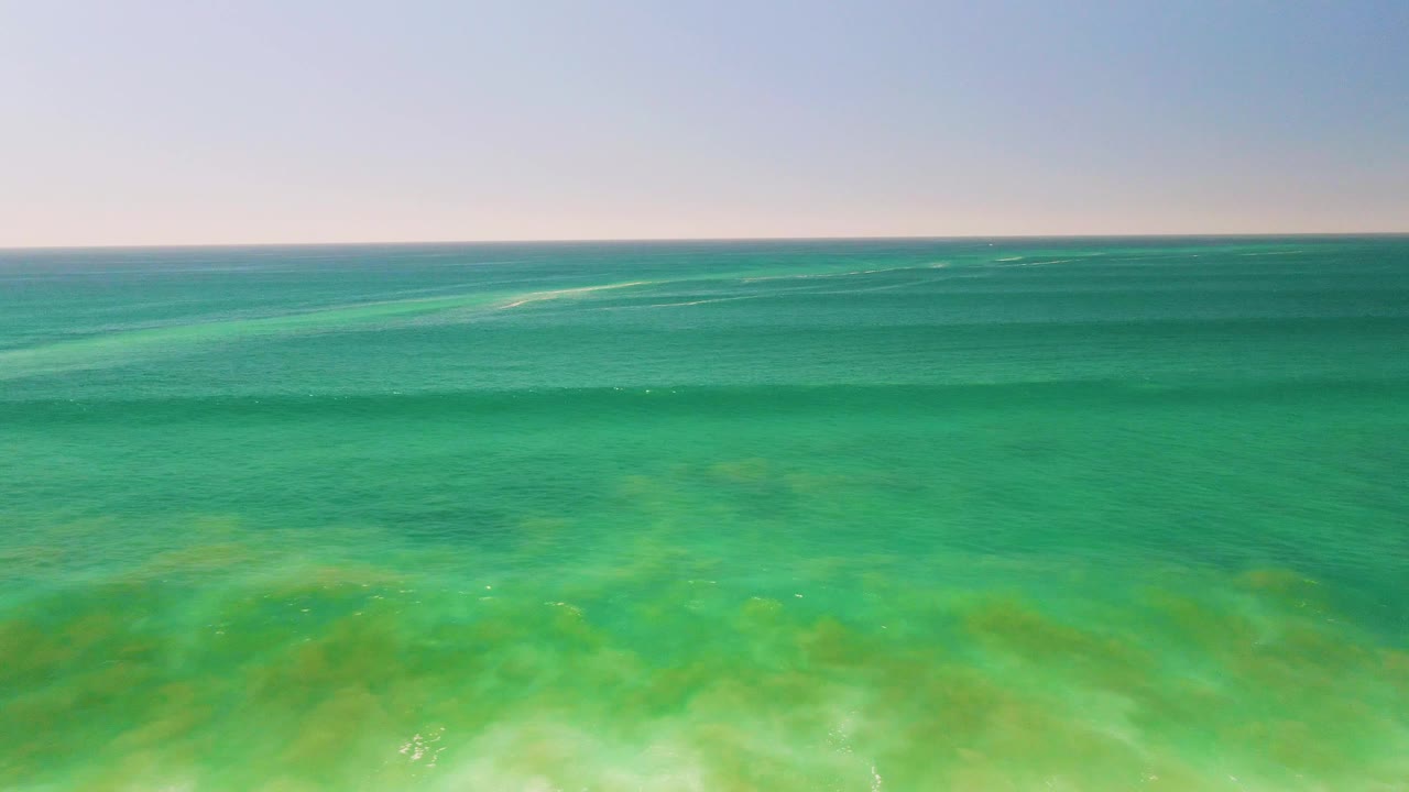 Wide view of transparent ocean water with green shallows and a level horizon.