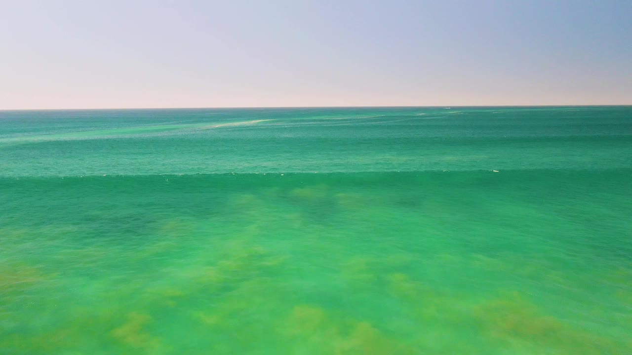 Mid-clip frame of shallow turquoise sea in San Jose del Cabo, with faint seabed patterns under the surface, low white wave marks near the horizon, and no visible people.