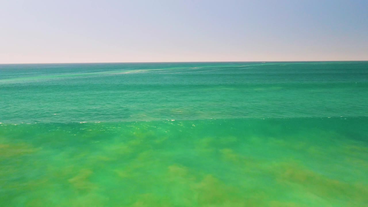 Wide drone-like view of shallow turquoise sea in San Jose del Cabo, Mexico, with a soft darker wave band across the middle and no visible people.