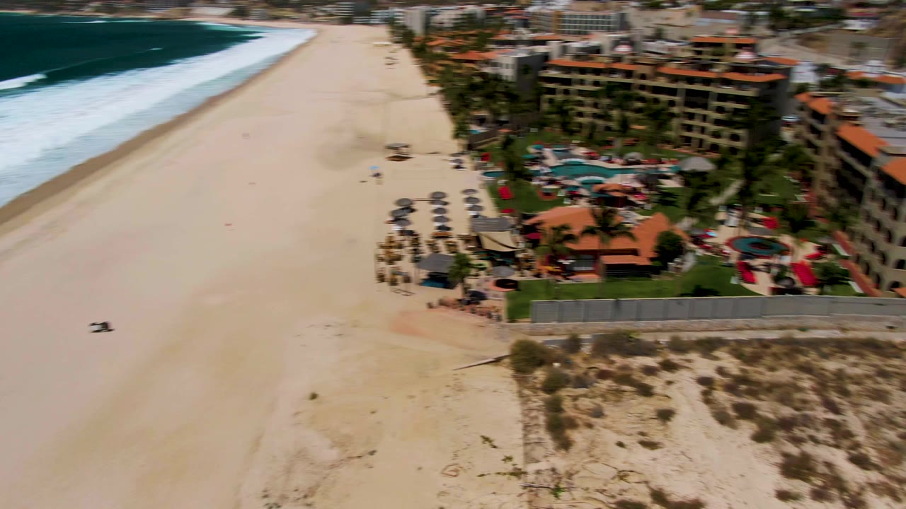 Aerial beach view with resort buildings entering frame