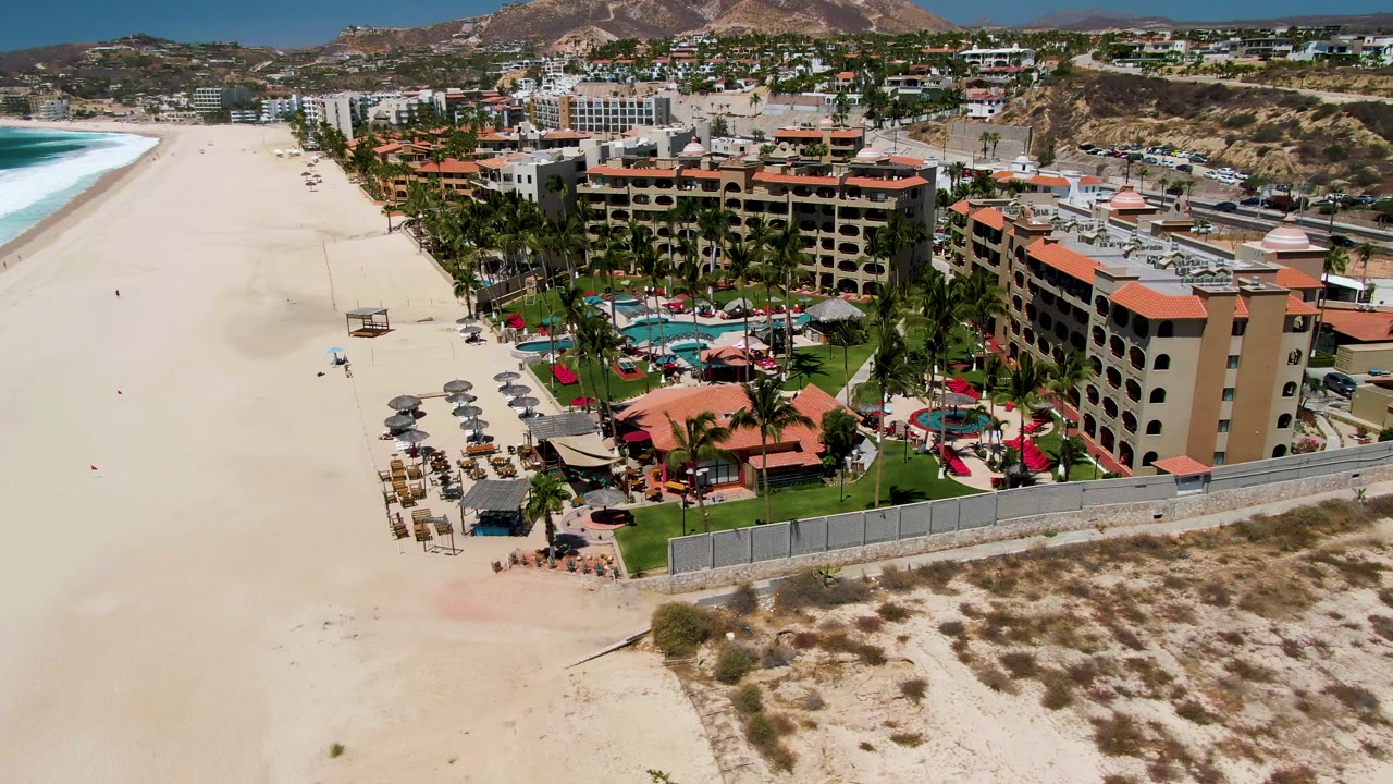 High view of beach chairs, umbrellas, resort buildings, and surf.
