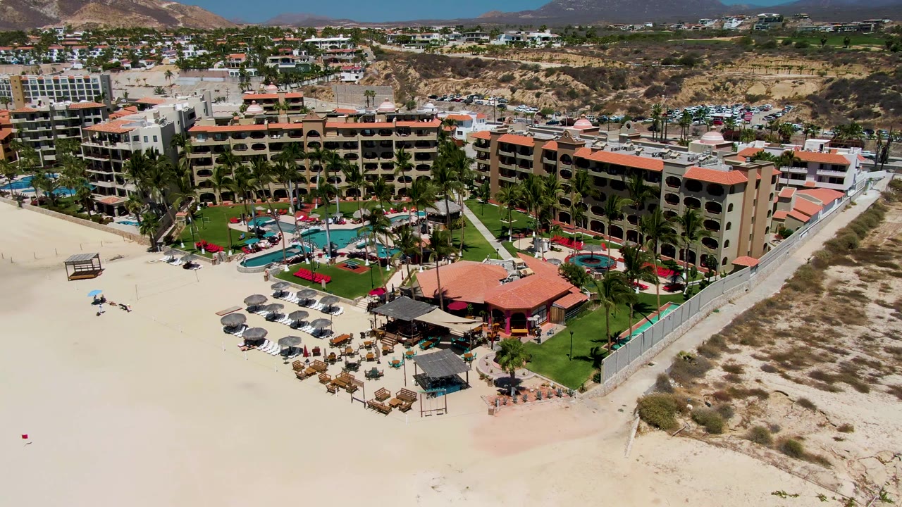Aerial beachfront resort view with pool courtyards, umbrellas, and sandy shoreline.
