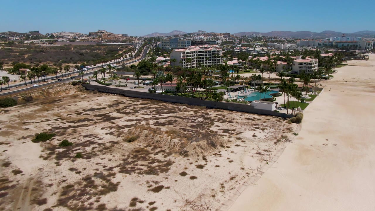Drone view over dunes and resort pool with road and coastal buildings beyond