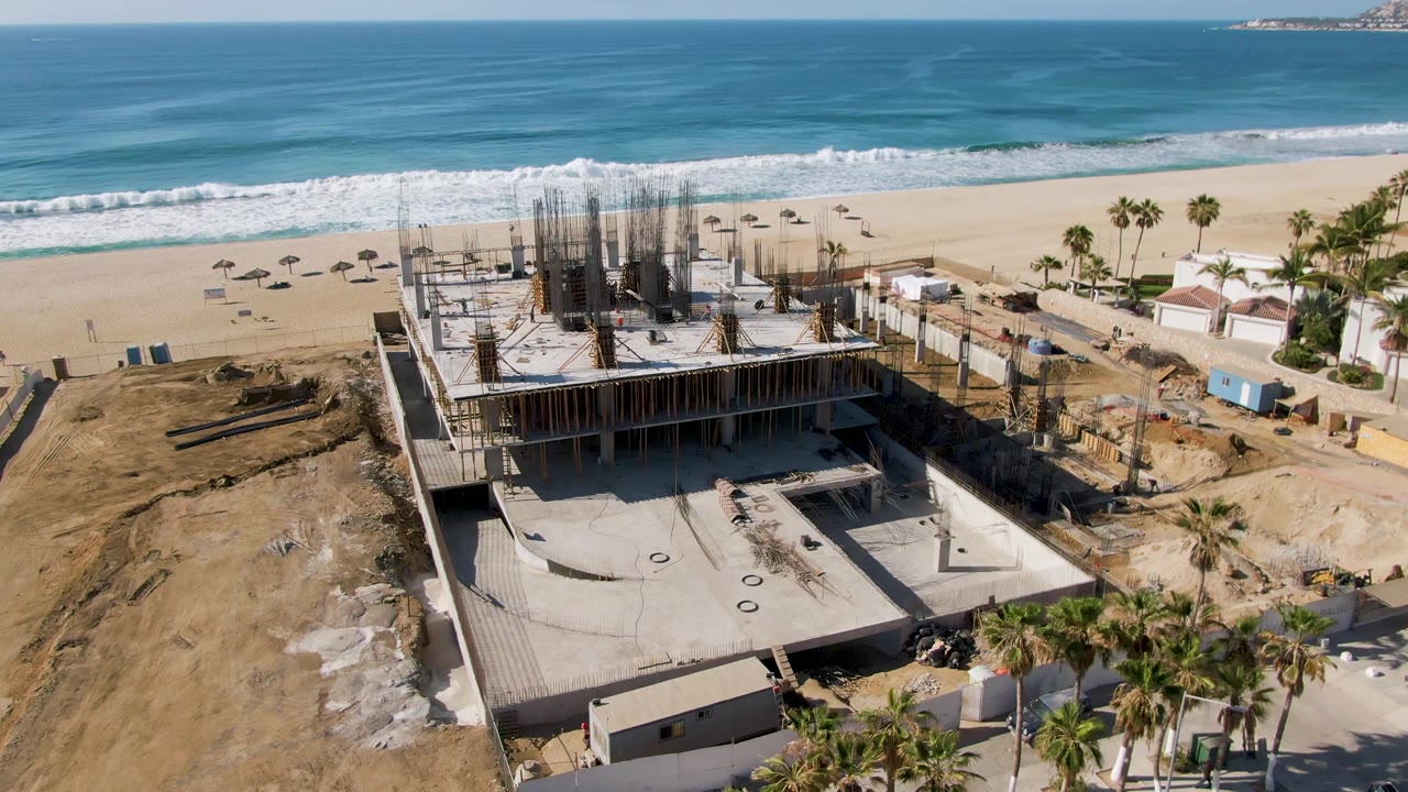 Aerial view of concrete beachside construction beside sand and ocean waves.