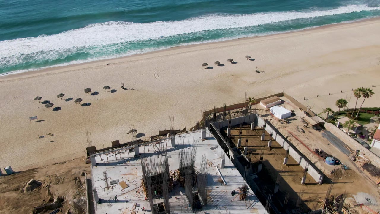 Aerial beach view with waves, umbrellas, sand, and partial construction site.