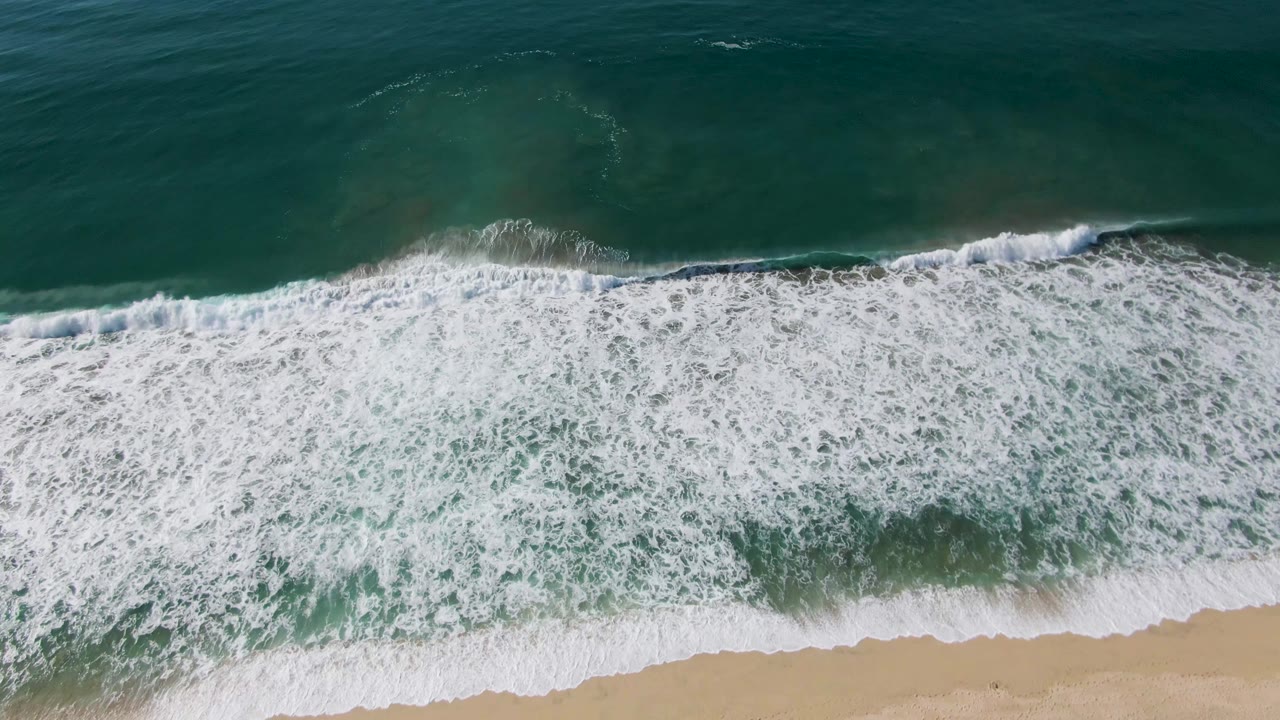 Overhead ocean foam spreads over the edge of a sandy beach
