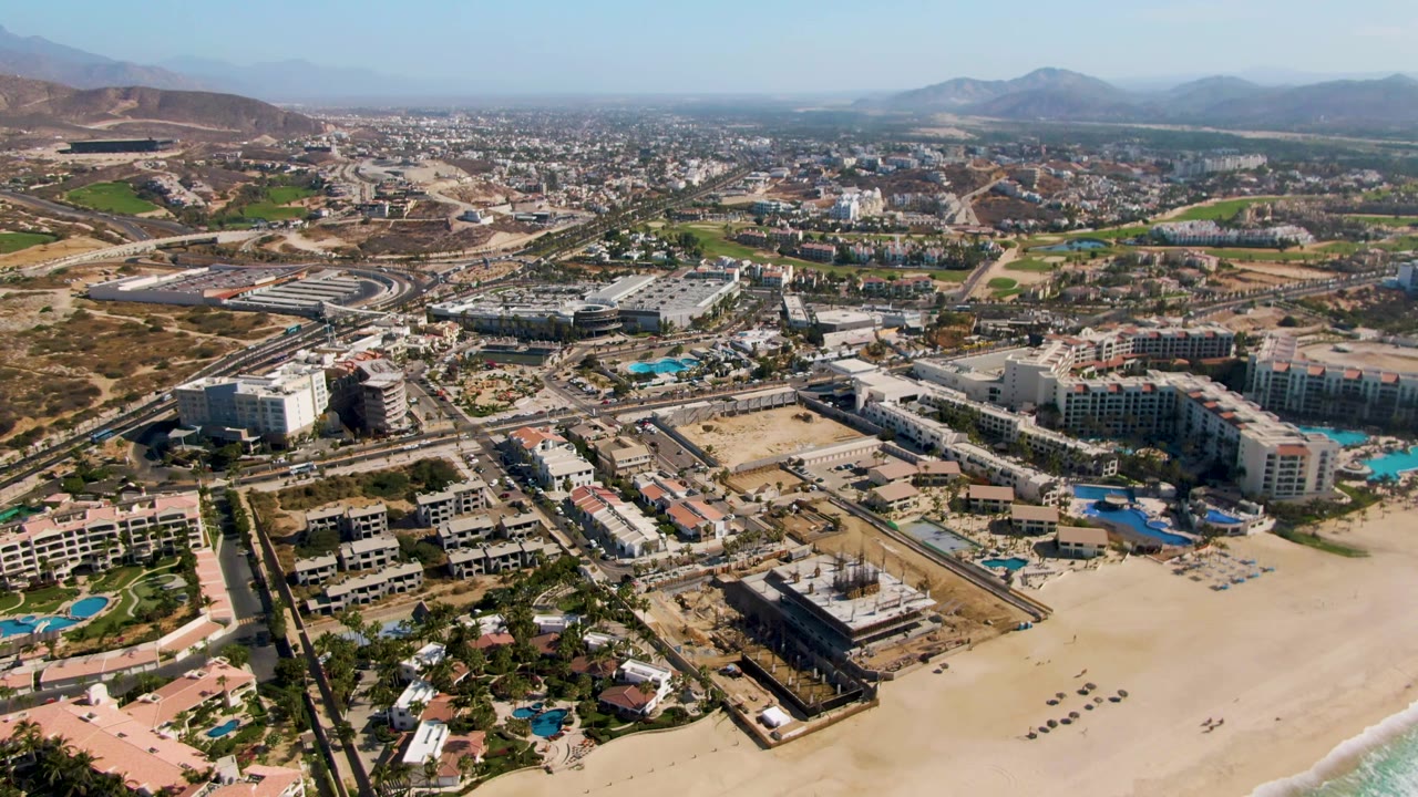 Aerial resort coastline with sandy beach, hotels, pools, and dry hills