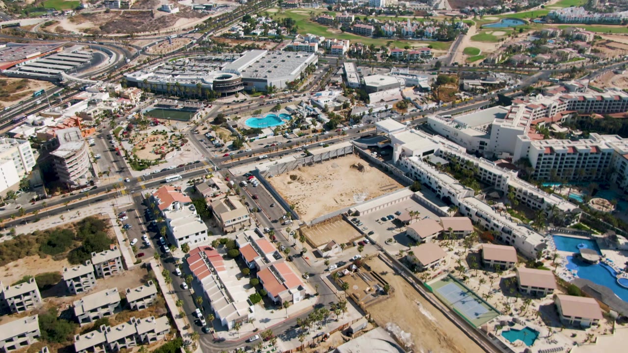 Drone view over resort-area buildings, road grid, pools, and open dry land.