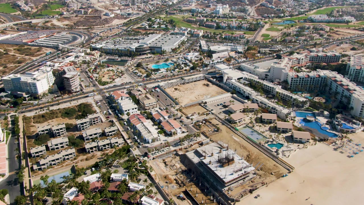 Aerial view of coastal buildings, sandy beach, roads, pools, and construction areas.