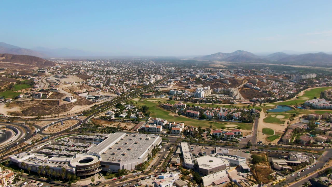 Aerial frame of roads, urban buildings, golf course, and mountain horizon.
