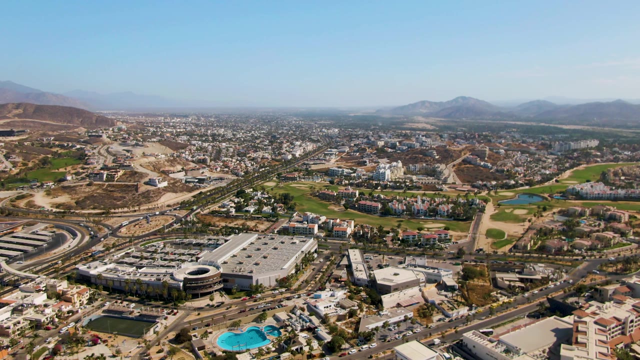 Aerial cityscape with foreground buildings, roadways, green spaces, and hills