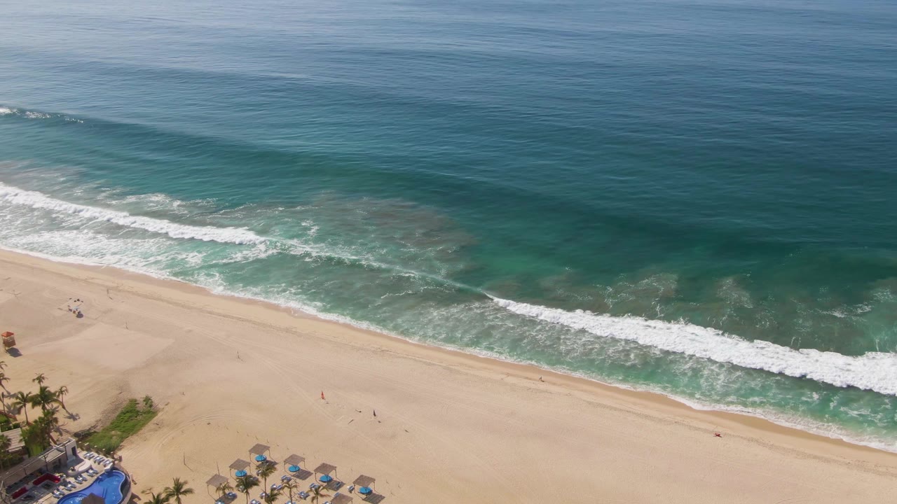Overhead coastline view with white surf rolling toward pale sand