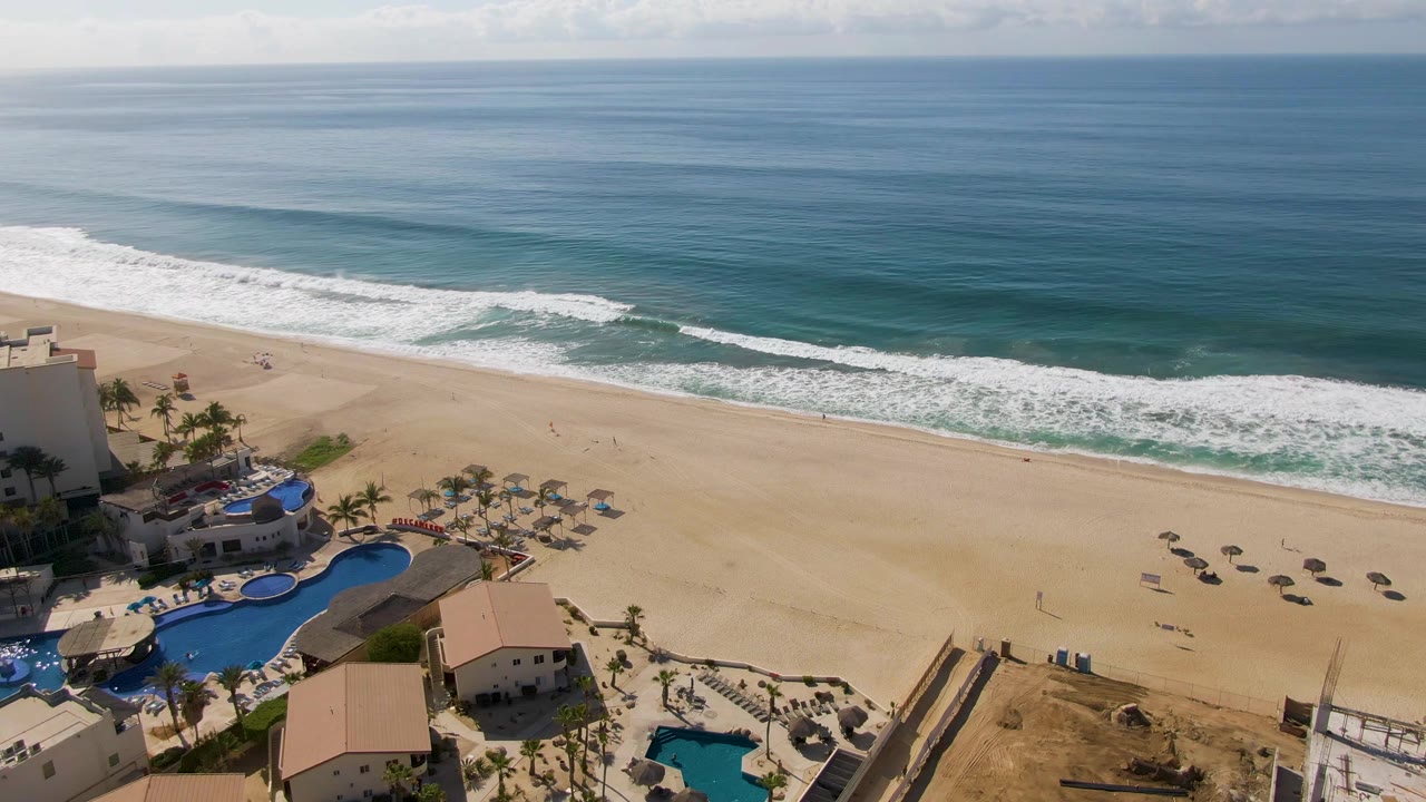 Wide beach and surf with resort pools and palms in the lower corner.