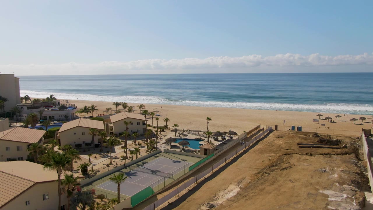 Aerial coastal resort view with bare ground, tennis courts, pools, beach, and ocean.