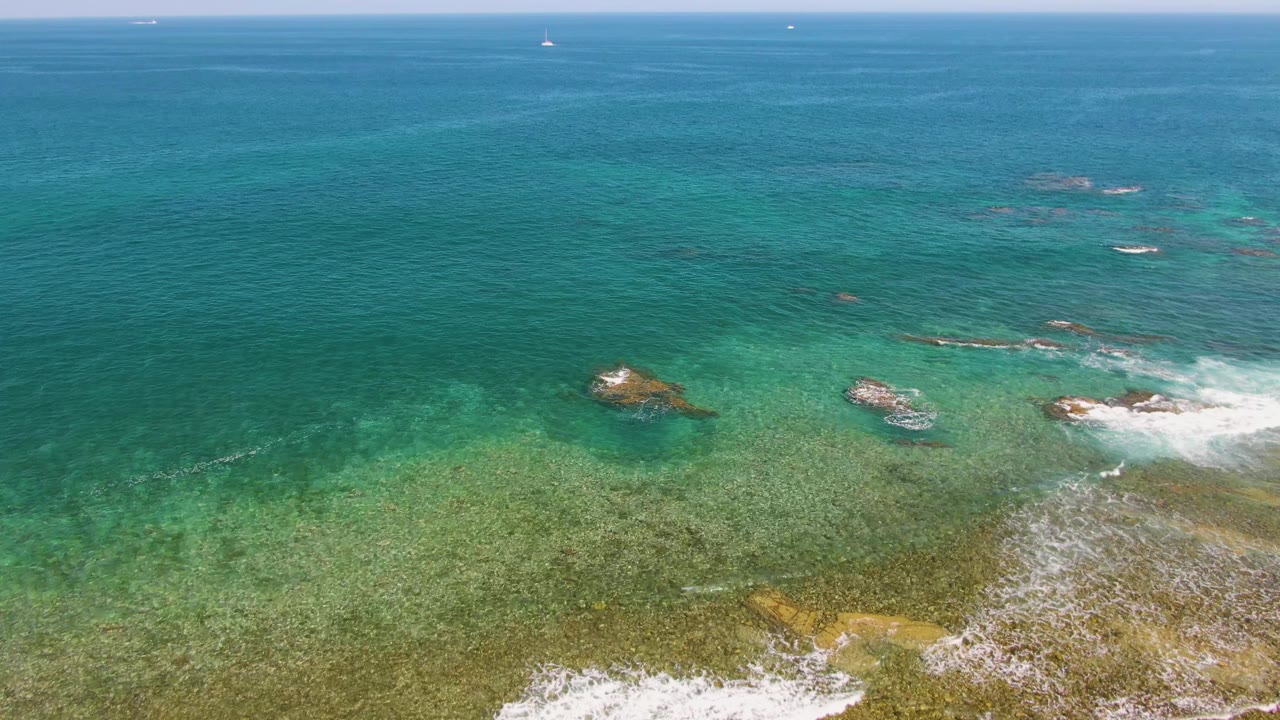 Clear ocean water with white waves curling over a rocky shelf.