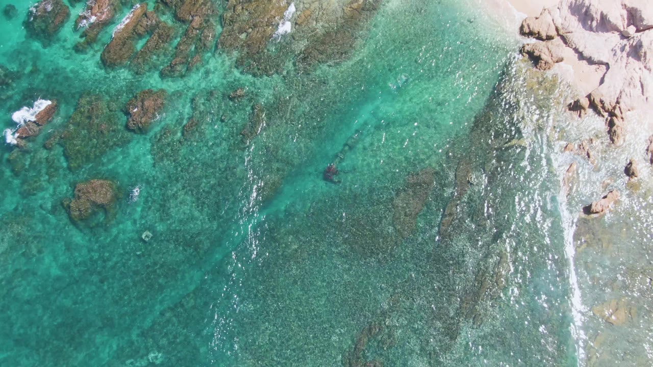 Overhead turquoise water beside rocks and pale sand
