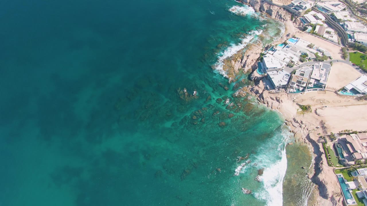 Aerial coastline with broad ocean and rocky surf near buildings