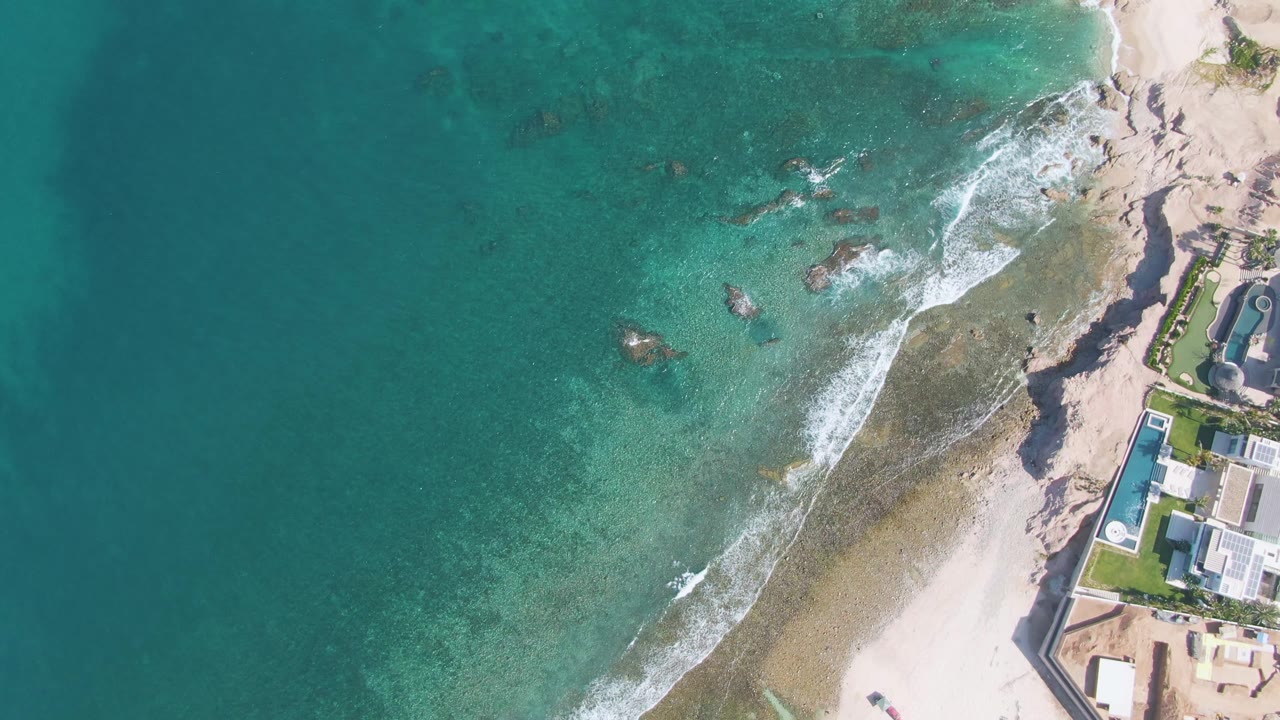 Clear ocean water and white foam cross a sandy shoreline beside beachside buildings.