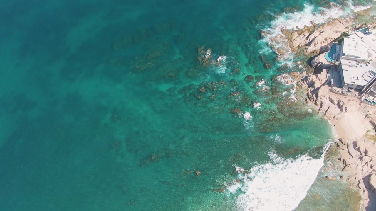 Overhead surf breaking over rocks in clear blue-green water.