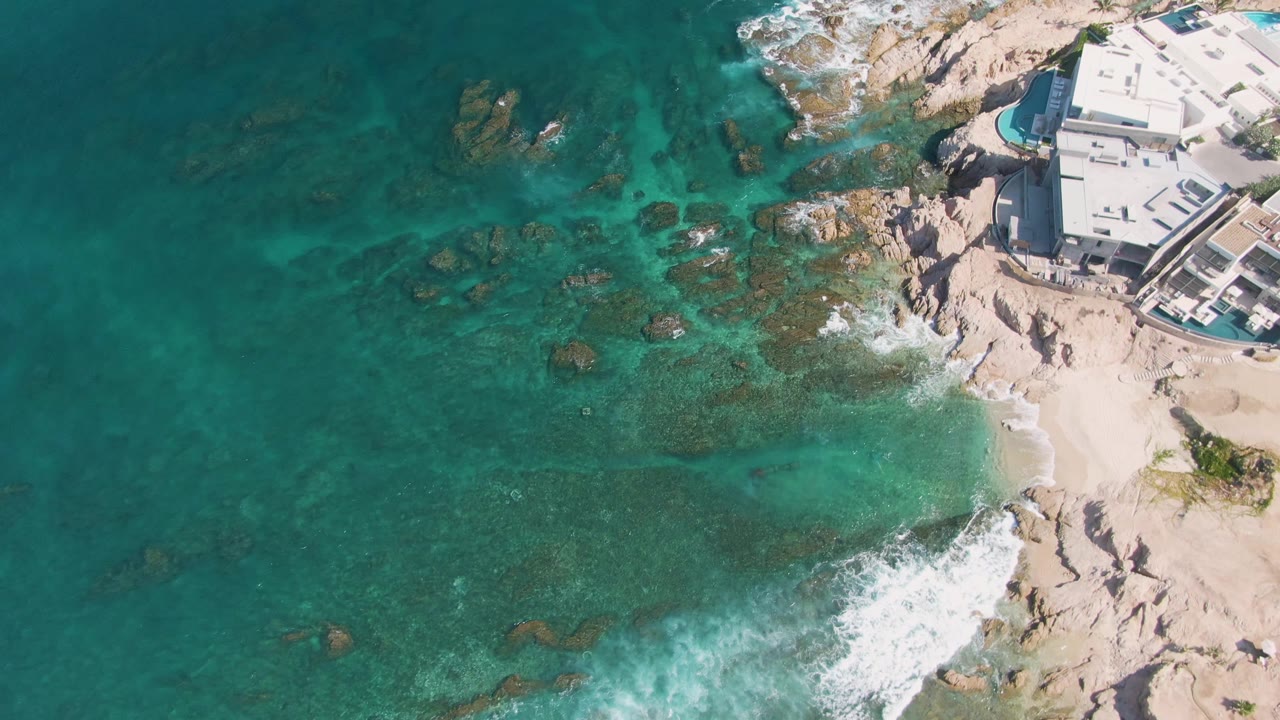 Overhead coastline with clear sea, reef rocks, breaking surf, and building.